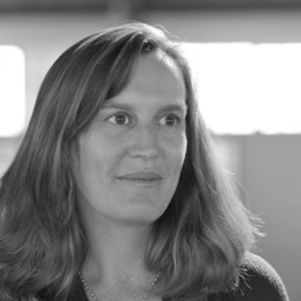 A woman with shoulder-length hair looks slightly to the side, smiling softly. The background is out of focus, and the image is in black and white.